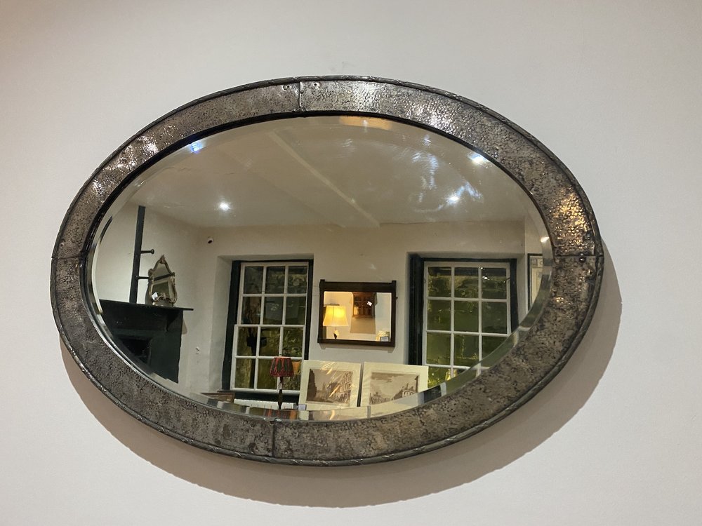 EARLY 20TH CENTURY OVAL MIRROR IN HAMMERED METAL FRAME WITH EMBOSSED DECORATION